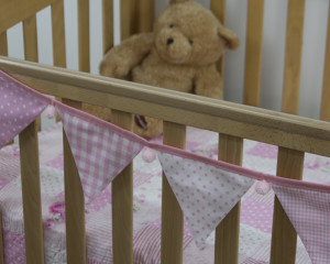 Baby pink bunting with pink pom-poms on cot