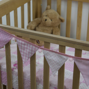 Baby pink bunting with pink pom-poms on cot